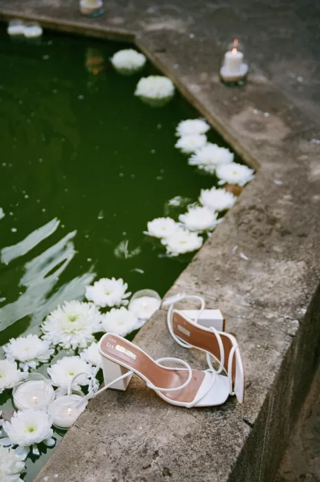Bridal heels resting beside a candlelit pond with floating white flowers at Finca Es Convent.
