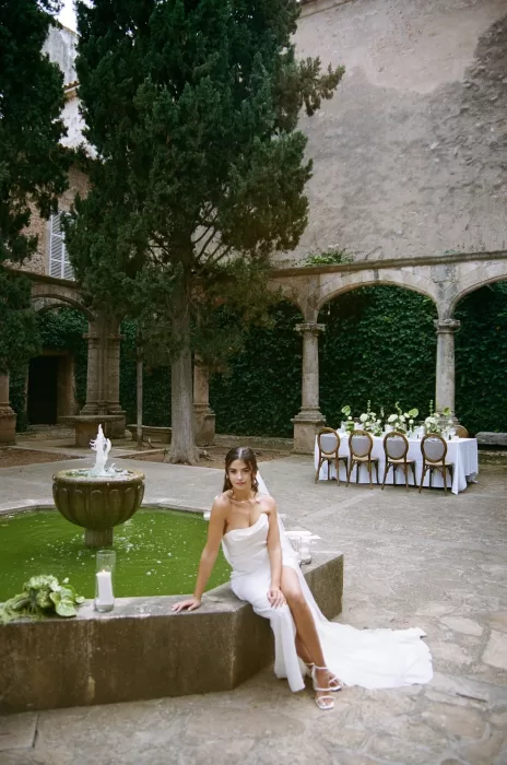Bride seated by the courtyard fountain at Finca Es Convent, with reception tables set in the background.