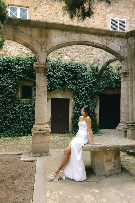 Bride seated within the historic stone cloister courtyard at Finca Es Convent, surrounded by ivy-covered arches.