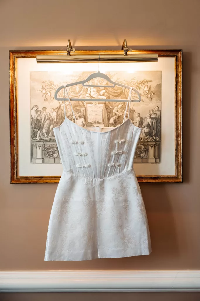 Short bridal dress hanging indoors at Finca La Concepción, captured in warm ambient light.