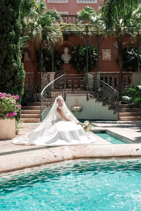 Bride seated beside the turquoise pool at Finca La Concepción, framed by palm trees and elegant courtyard architecture.