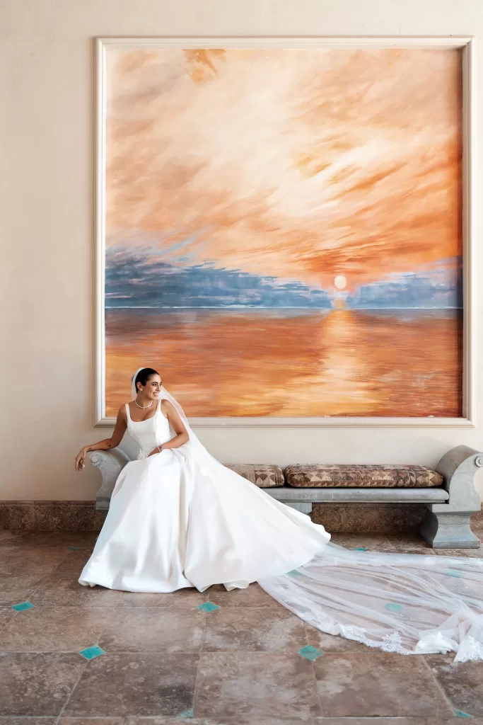 Bride seated indoors beneath a large sunset artwork at Finca La Concepción, her train flowing across the floor.