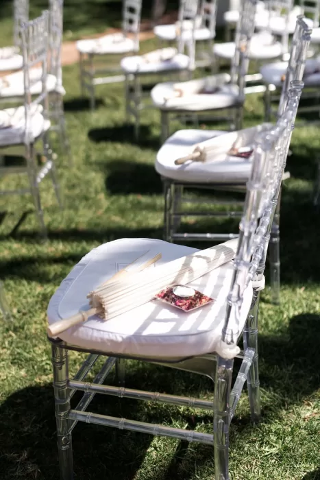Transparent ceremony chairs arranged on the lawn at Finca La Concepción with fans placed for guests.