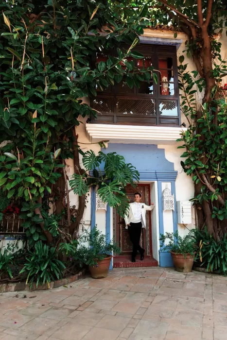Groom standing in a leafy courtyard doorway at Finca La Concepción, framed by climbing greenery and potted plants.