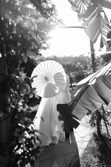 Bride and groom walking together with a parasol through lush garden paths at Finca La Concepción.