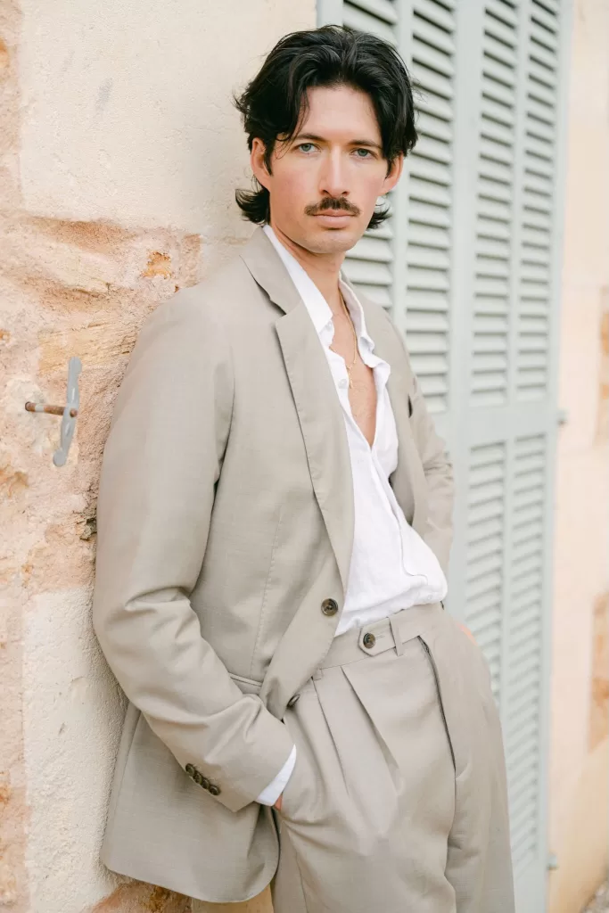 Groom portrait at Fontsanta leaning against the stone walls and shutters, styled in a relaxed modern wedding look.