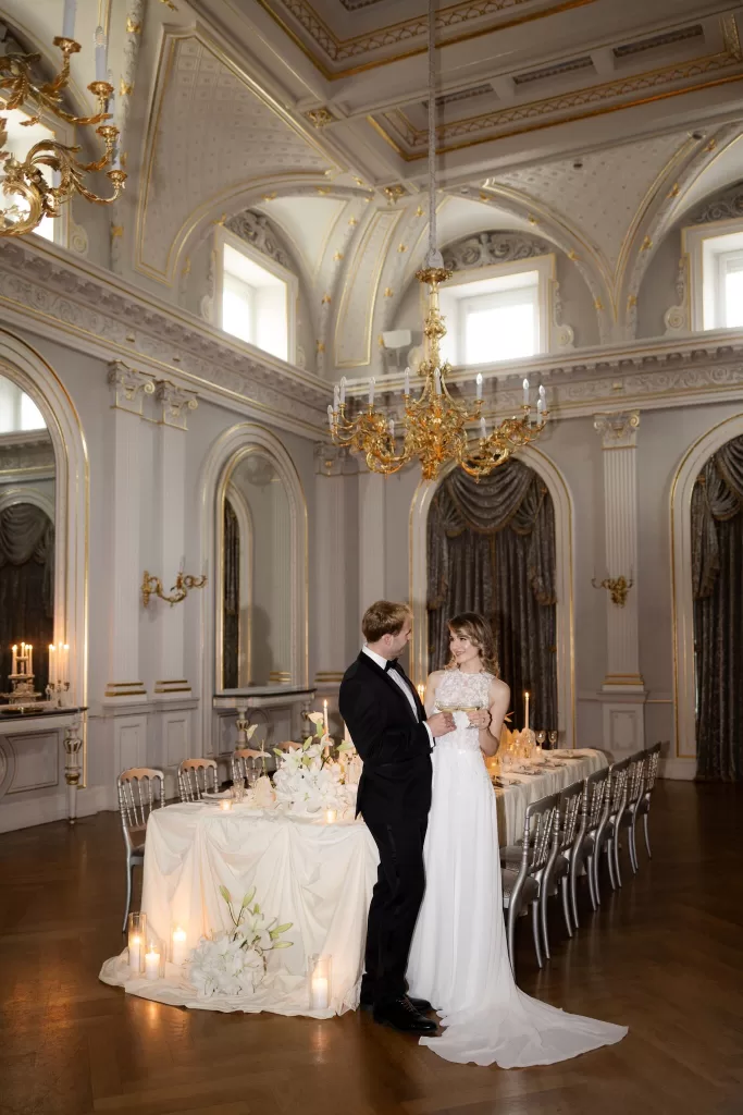 Bride and groom standing together inside the ornate ballroom at Grand Hotel du Lac, surrounded by chandeliers, candlelight and classical detailing.