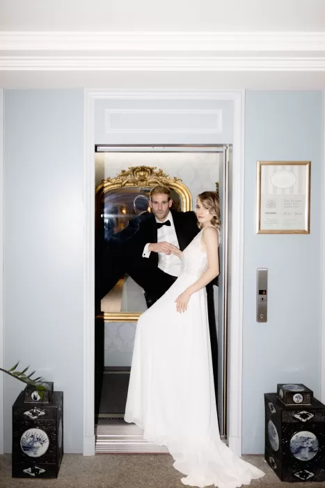 Bride and groom posing inside a vintage elevator at Grand Hotel du Lac, blending modern fashion with classic hotel charm.
