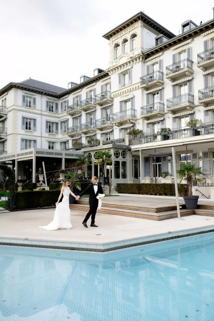 Bride and groom walking hand in hand beside the pool at Grand Hotel du Lac, framed by the elegant historic facade.