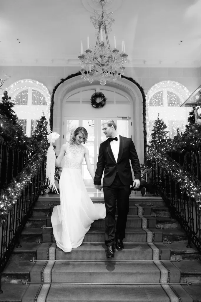 Bride and groom descending the grand staircase at Grand Hotel du Lac, illuminated by festive lights and winter greenery.
