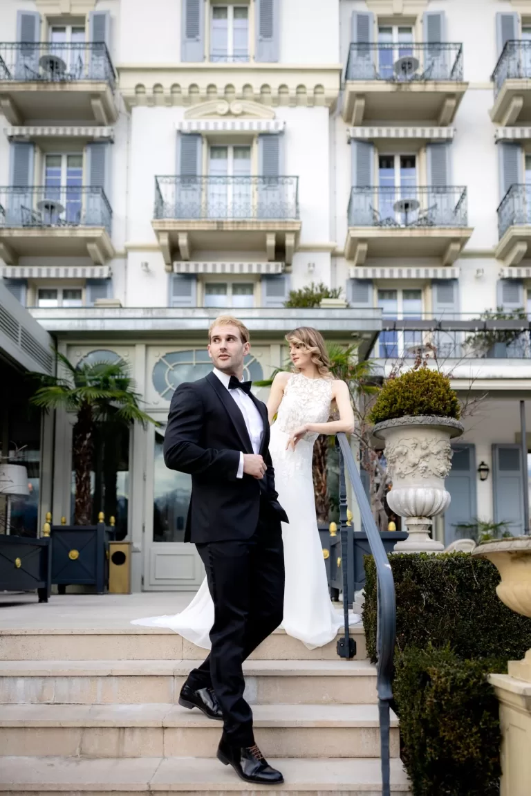 Bride and groom posing on the steps of Grand Hotel du Lac, with the historic balconies and elegant entrance as their backdrop.