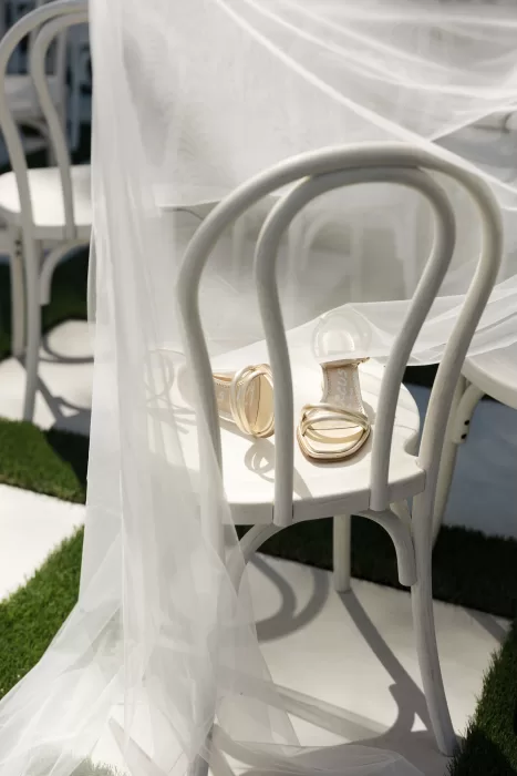 Bridal shoes rest on a white chair beneath flowing veil fabric at The Greenhouse at Arrows Farm.