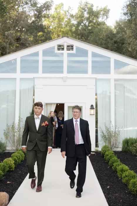 Wedding guests exit the greenhouse ceremony space at The Greenhouse at Arrows Farm, surrounded by trees and soft daylight.