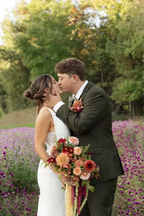 The couple kiss in a wildflower field at The Greenhouse at Arrows Farm, surrounded by soft purple blooms.