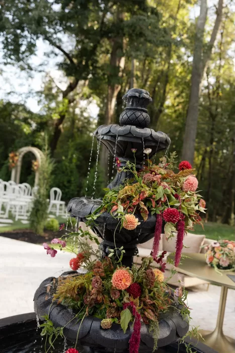 Floral arrangements cascade over a stone fountain at The Greenhouse at Arrows Farm, creating a romantic garden ceremony atmosphere.