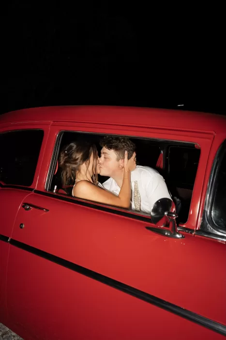 The couple share a kiss inside a vintage red car at The Greenhouse at Arrows Farm at night.