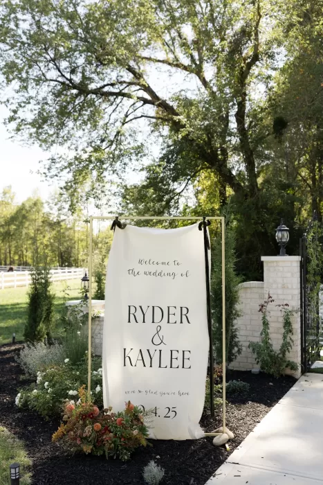 A wedding welcome sign displayed at the entrance of The Greenhouse at Arrows Farm, styled with florals and greenery.