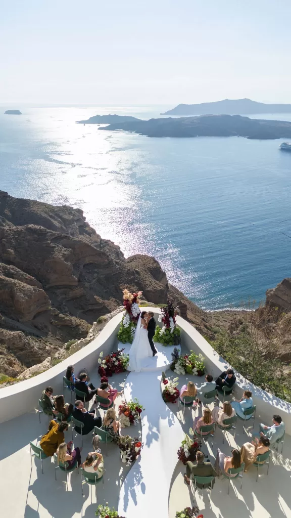Aerial view of a cliffside wedding ceremony at Islet Santorini, with guests seated around a sculptural aisle above the caldera.