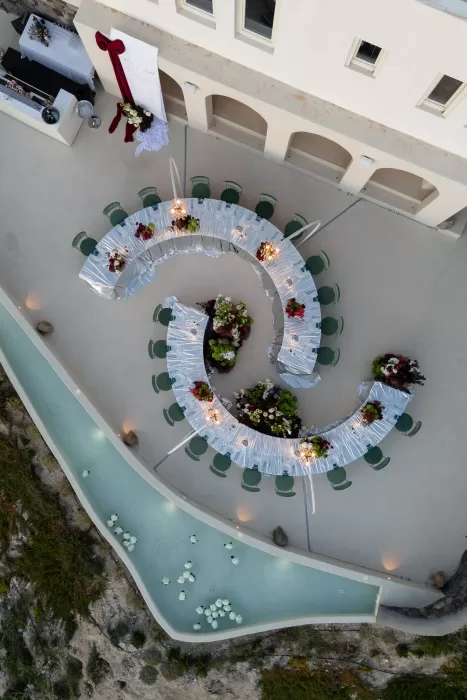 Overhead view of a curved wedding reception layout with floral installations and water features at Islet Santorini.