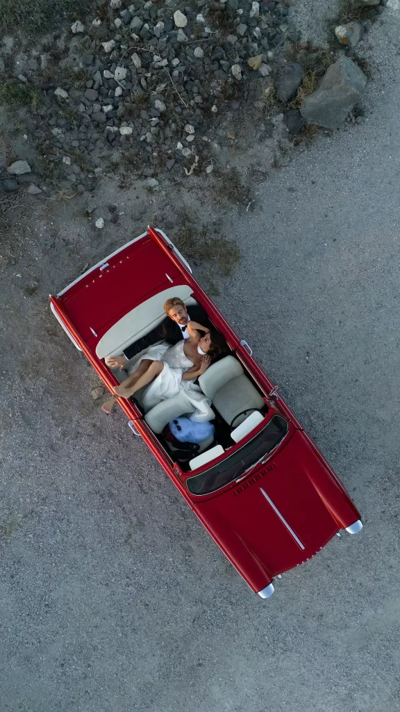 Bride and groom photographed from above in a red convertible during their wedding at Islet Santorini.