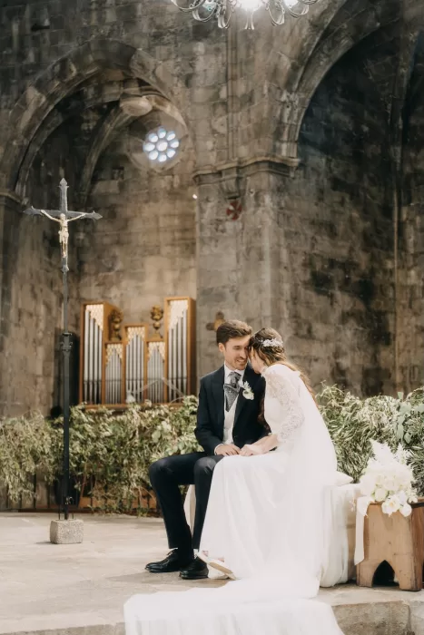Bride and groom sharing a quiet, intimate moment seated at the altar during their church ceremony near Mas de Les Voltes.