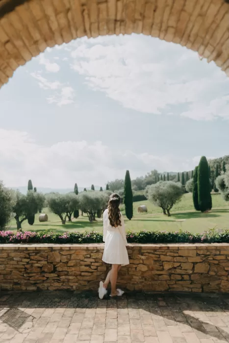 Bride standing beneath a stone archway overlooking the olive groves and cypress trees at Mas de Les Voltes.