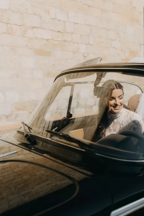 Bride smiling inside a vintage convertible outside the stone walls of Mas de Les Voltes.