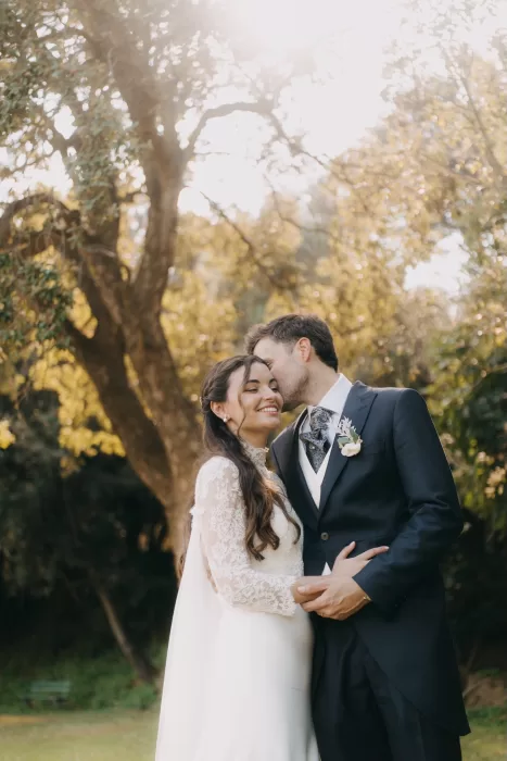 Couple embracing at golden hour in the gardens of Mas de Les Voltes, surrounded by warm light and mature trees.