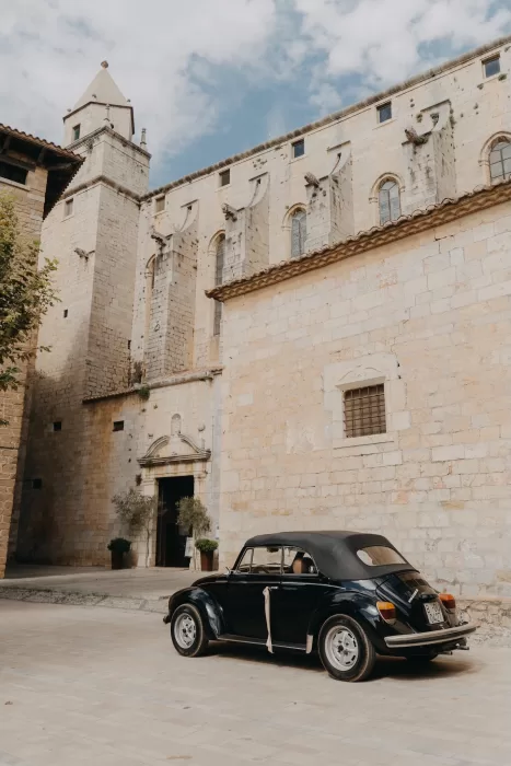 Vintage wedding car parked outside the historic stone entrance of Mas de Les Voltes, highlighting the venue’s old-world character.