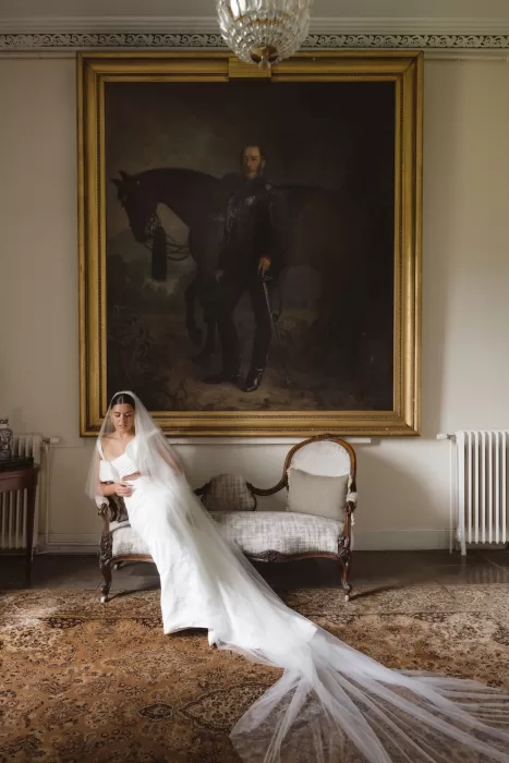 Bride seated beneath a grand portrait inside Boturich Castle, her veil trailing across the floor.