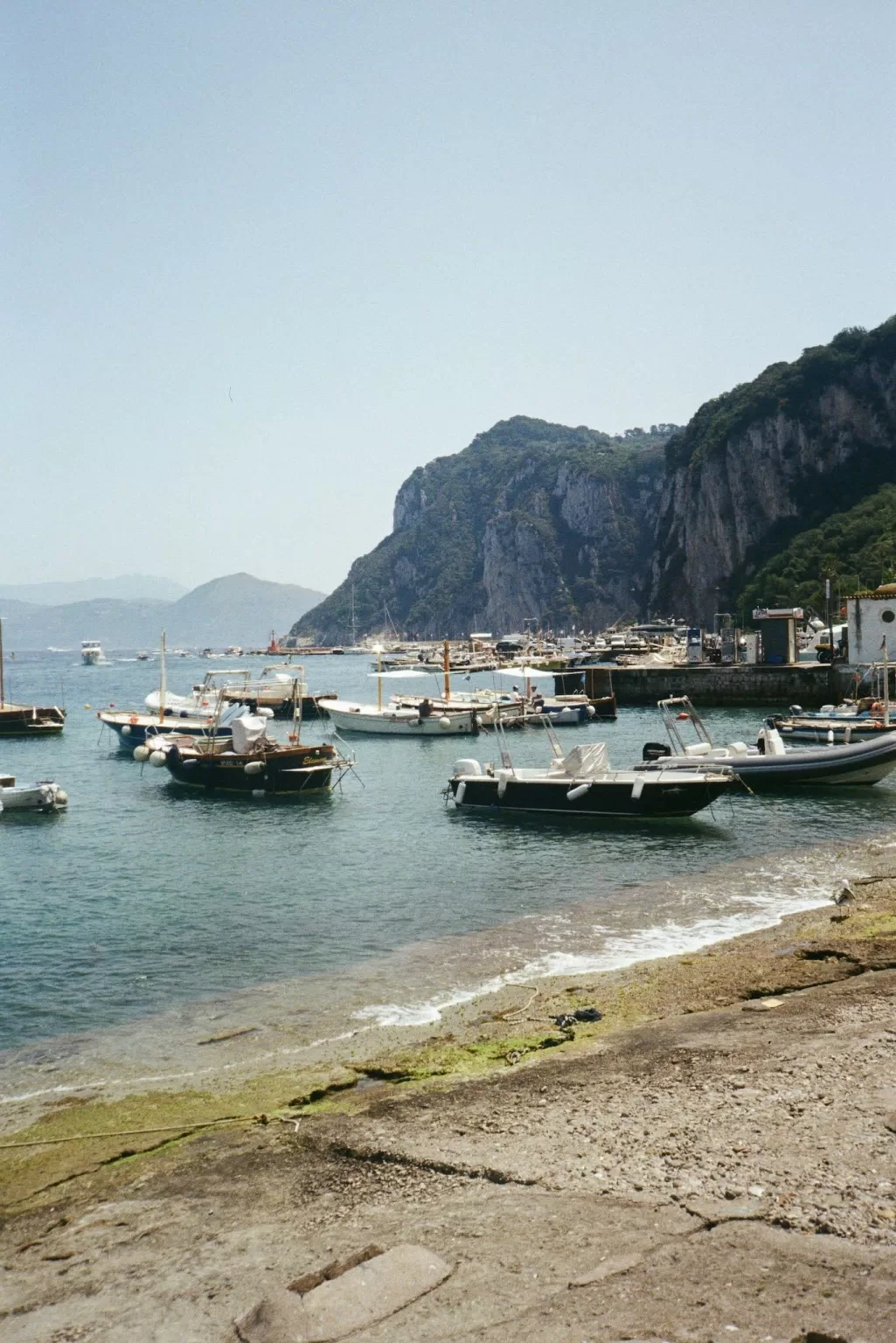 Boats floating in the crystal waters of Capri’s marina beneath rugged limestone cliffs.
