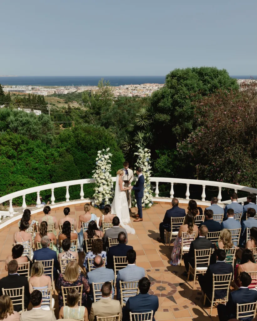 Bride and groom standing together beneath a white floral ceremony arch with countryside views at Casa Monte Cristo Collection.