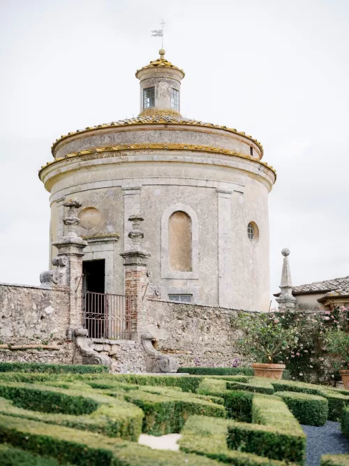 Ornate stone entrance and manicured Italian gardens at Castello di Celsa with sculpted hedges and blooming roses.