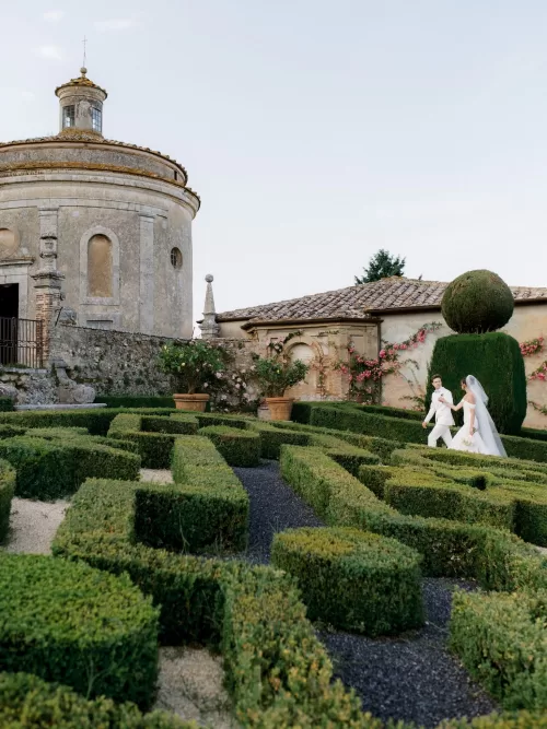 Bride and groom walking through the sculpted garden maze beside the chapel at Castello di Celsa.