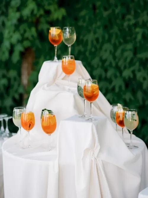 Aperol spritz cocktails displayed on draped white pedestals against ivy-covered walls at Castello di Celsa.