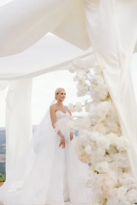 Bride standing beneath floral ceremony arch with sweeping Tuscan views at Castello di Velona.