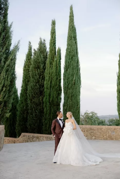 Bride and groom posing together among cypress trees at Castello di Velona.