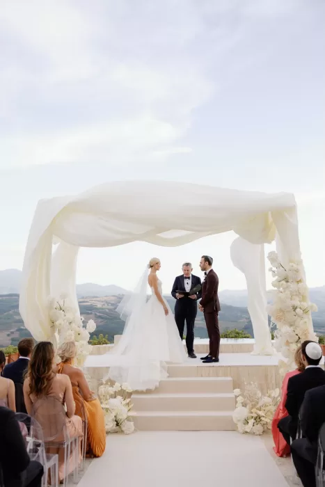 Outdoor wedding ceremony framed by white florals and rolling hills at Castello di Velona.