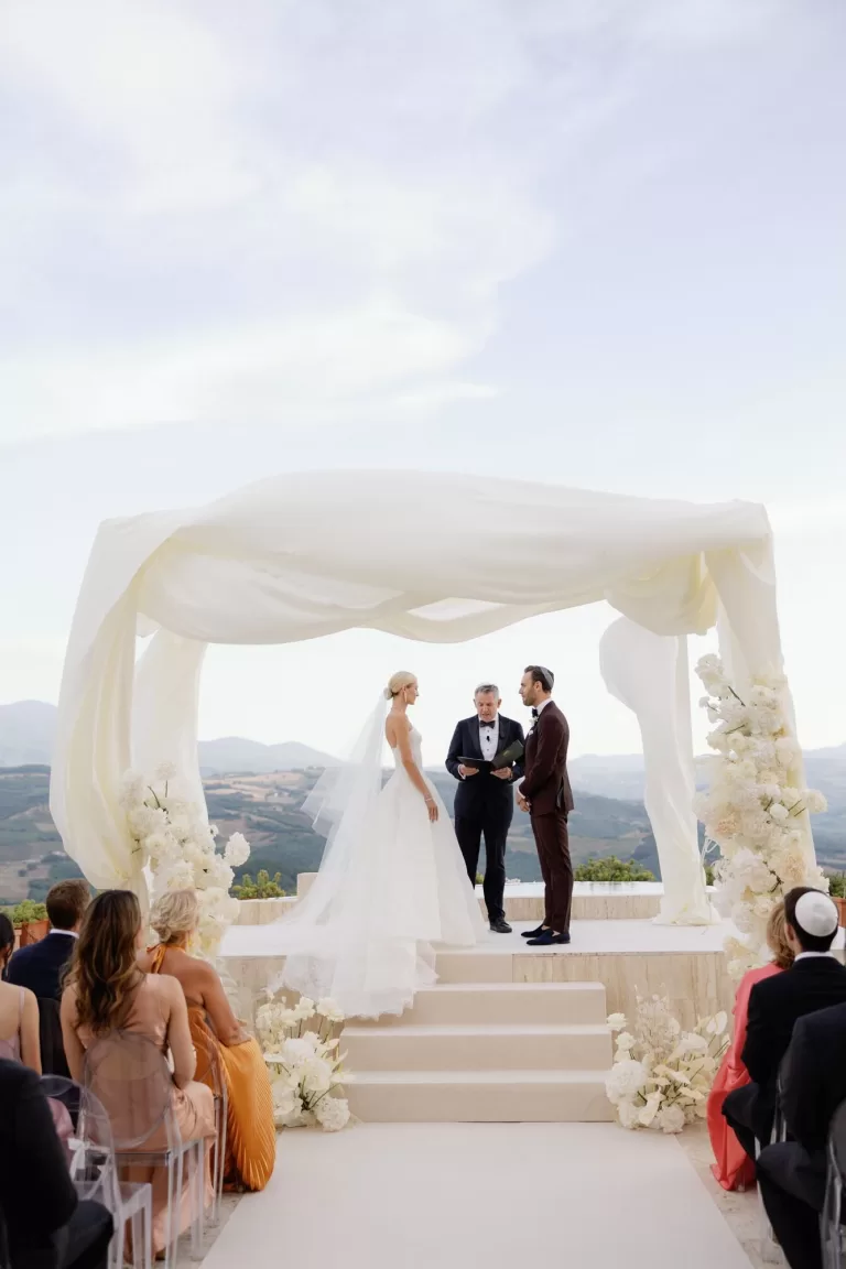 Outdoor wedding ceremony framed by white florals and rolling hills at Castello di Velona.