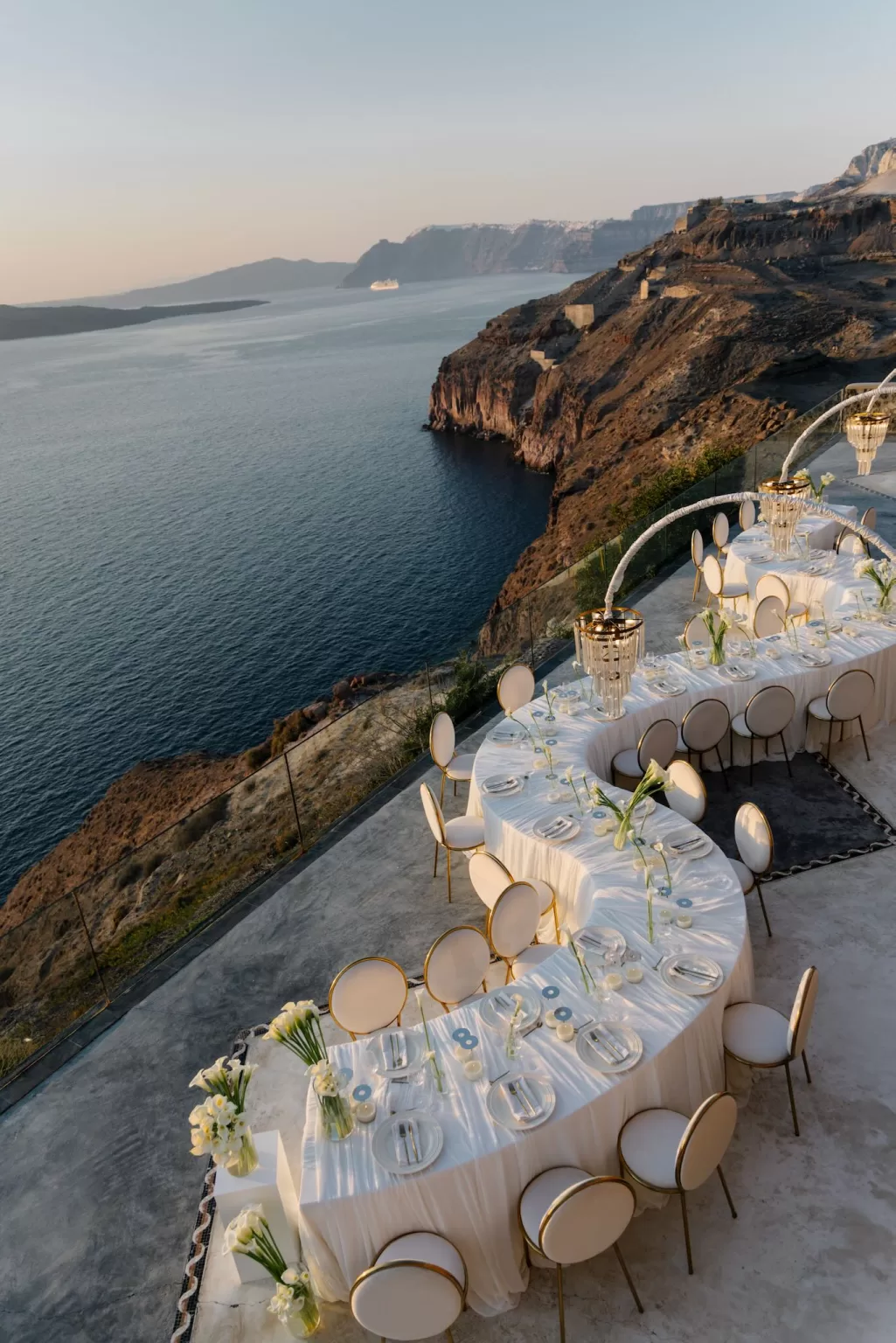 Elegant outdoor wedding reception at Cavo Ventus with sweeping caldera views, white table linens and sculptural lighting at golden hour.