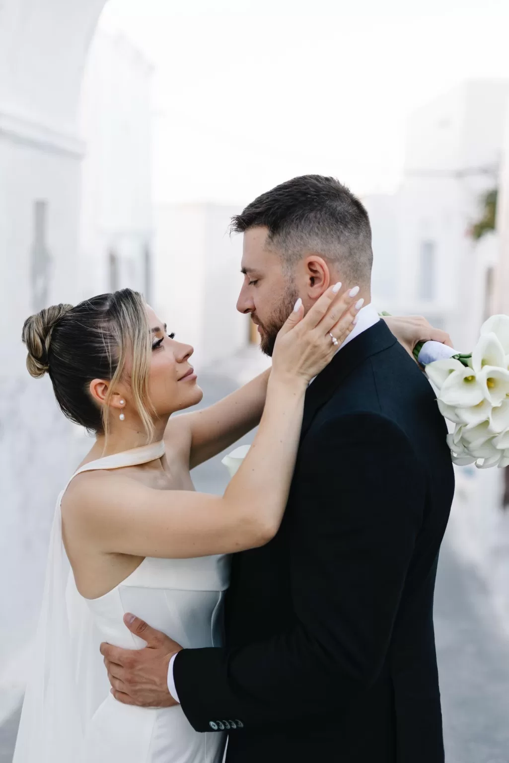 Intimate portrait of the bride and groom embracing in a whitewashed Santorini setting near Cavo Ventus.