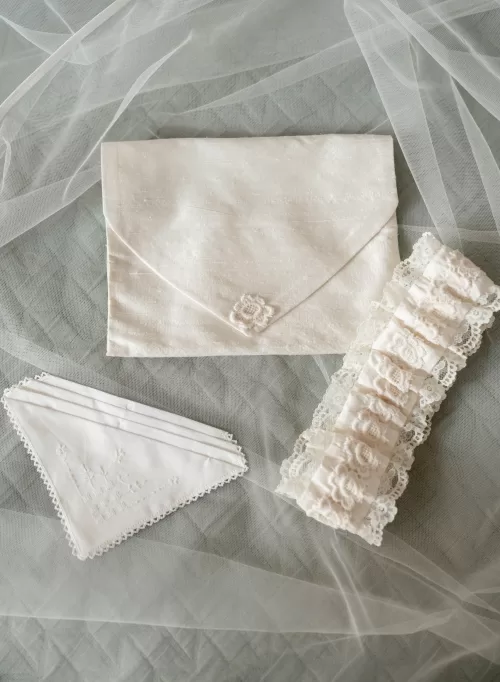 Delicate bridal accessories including embroidered handkerchief, lace garter and silk envelope arranged on soft veil fabric at Château Canet.