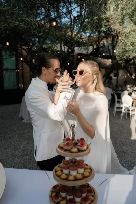 Bride and groom in sunglasses enjoying champagne during cocktail hour at Château Canet, surrounded by olive trees and soft evening string lights.