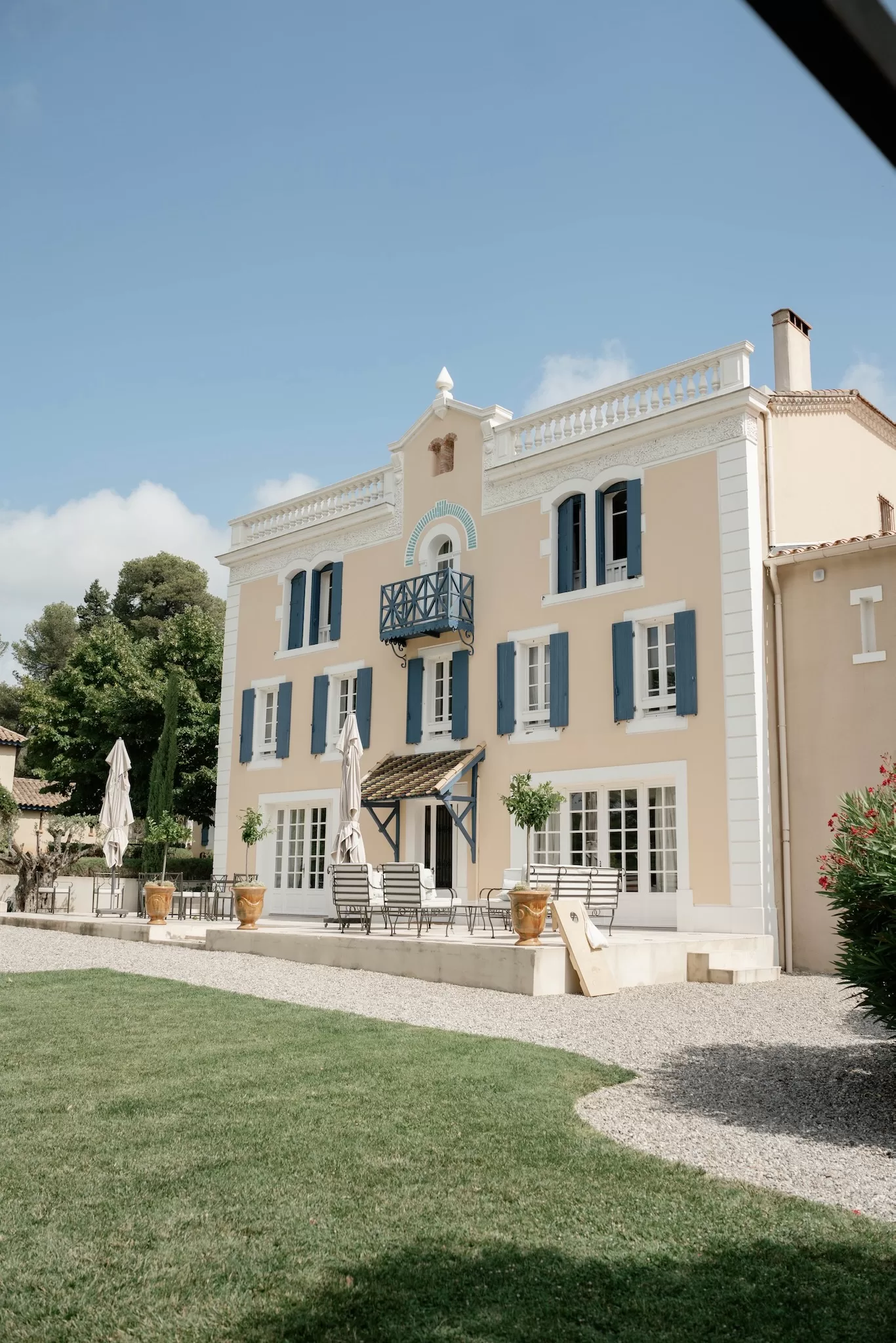 Full exterior view of Château Canet with cream stone walls, blue shutters and wrought iron balcony overlooking the gravel terrace.