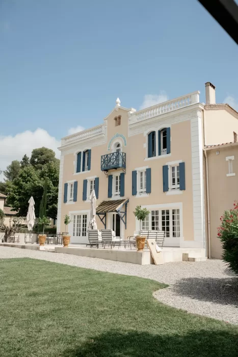 Full exterior view of Château Canet with cream stone walls, blue shutters and wrought iron balcony overlooking the gravel terrace.