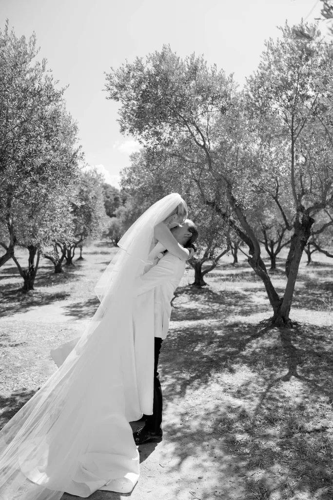 Black and white portrait of the bride and groom in the olive grove at Château Canet, the veil sweeping across sun-dappled ground.