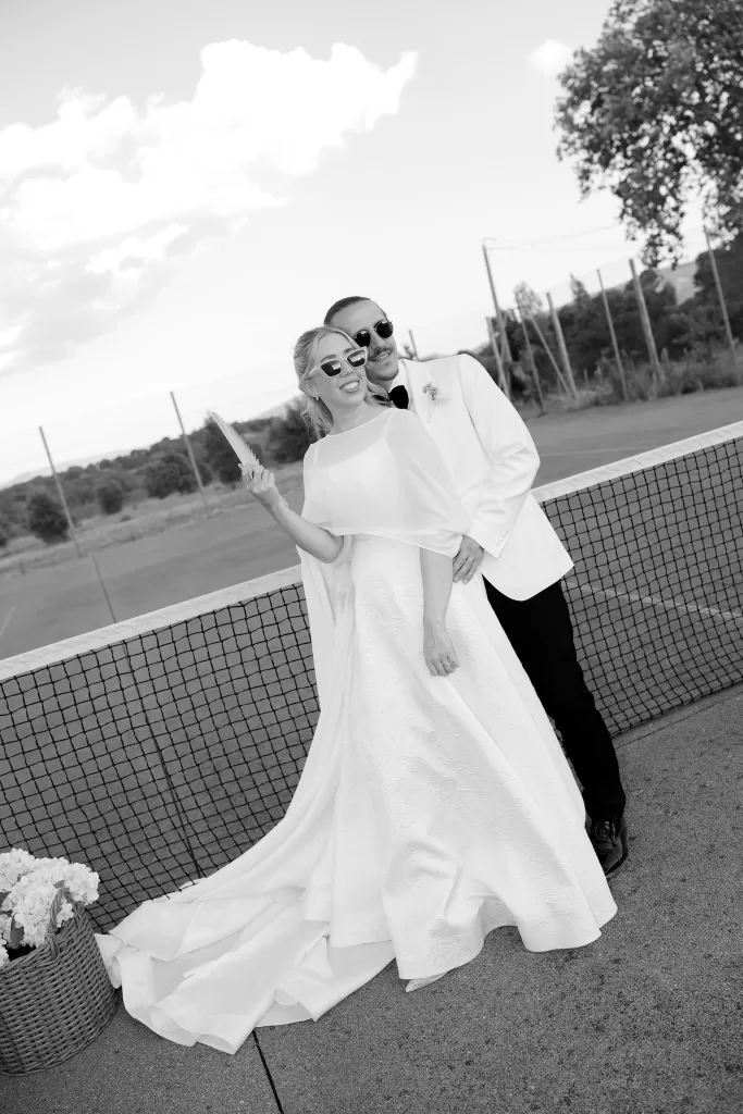 Bride and groom posing playfully on the Château Canet tennis court at golden hour, with countryside views stretching behind them.