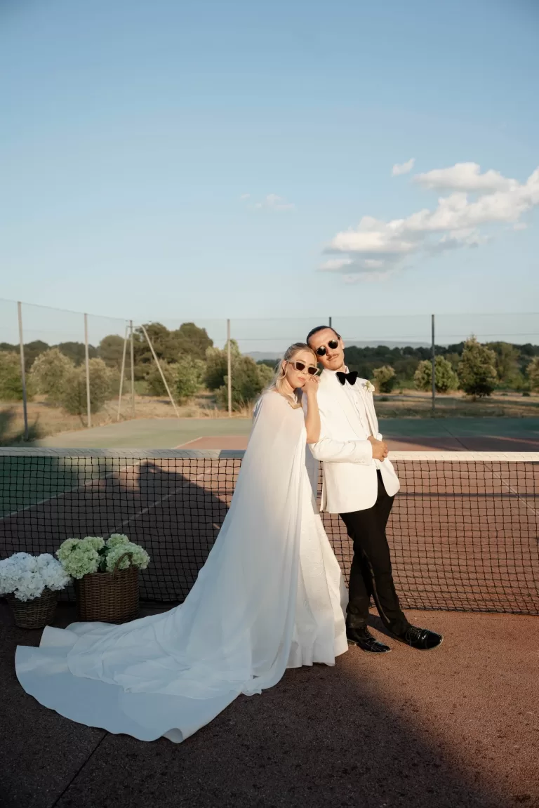 Bride and groom posing playfully on the Château Canet tennis court at golden hour, with countryside views stretching behind them.
