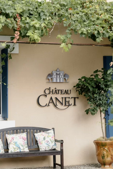 Château Canet wall signage beneath trailing vines, with a wooden bench and potted citrus tree adding Provençal charm to the courtyard setting.