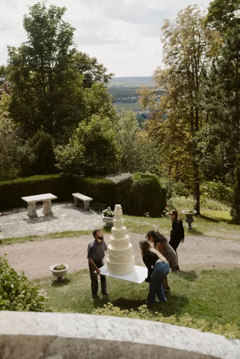Wedding team carefully carrying a large tiered cake through the gardens of Château du Prieuré d’Evecquemont.